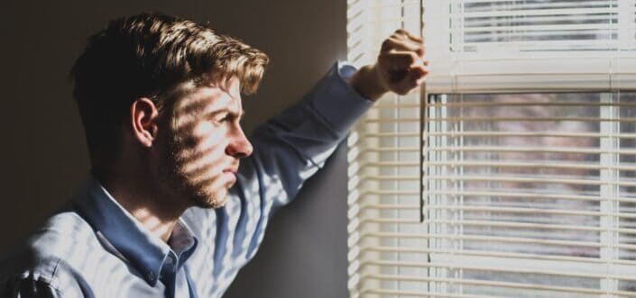 Man looking outside through the window with blinds