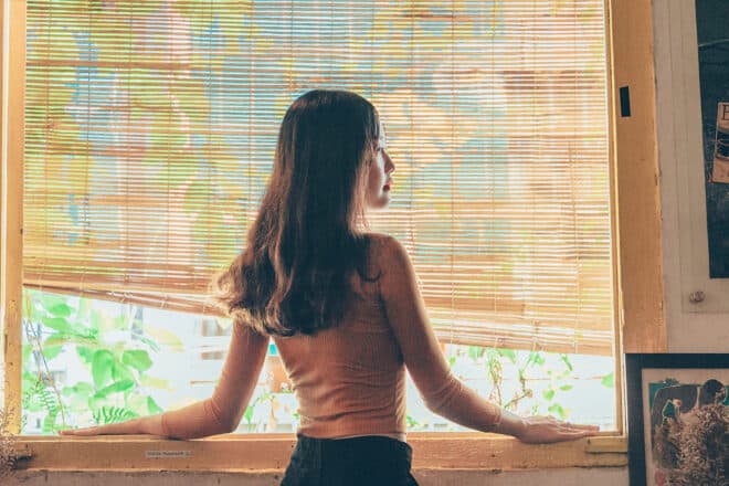 Woman peaking through the window with blinds - types of blinds