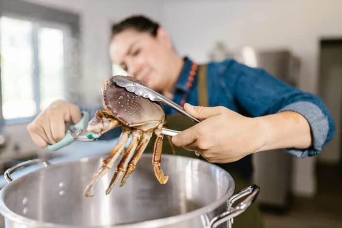 Woman holding cooked crab with kitchen pincers 
