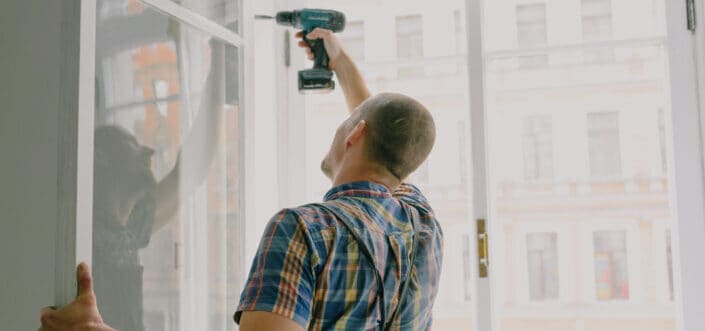 Handyman installing window frame with drill in house