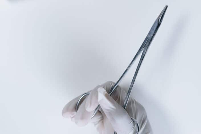 Person with white gloves holding forceps