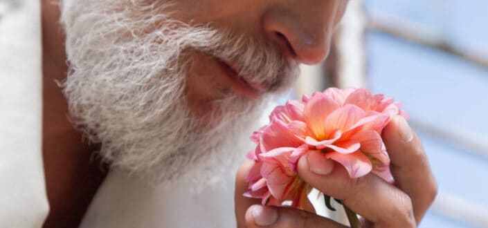 An elderly man smelling a pink flower